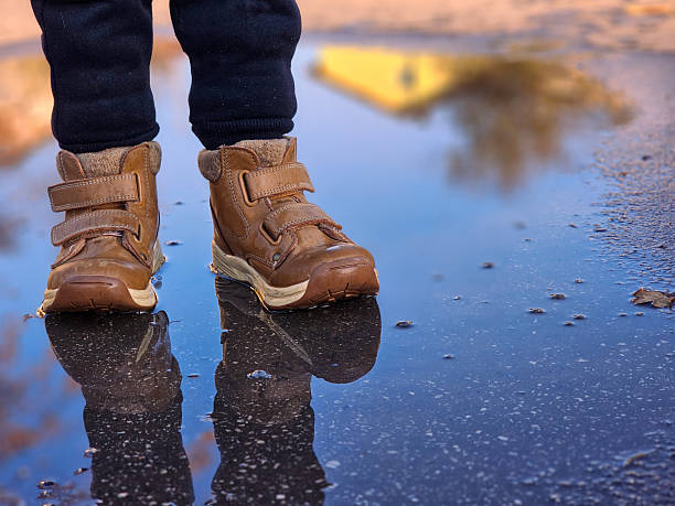 istock Child’s brown boots walking through puddles. 2234527357