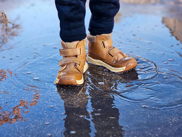 istock Child’s brown boots walking through puddles. 2234527417