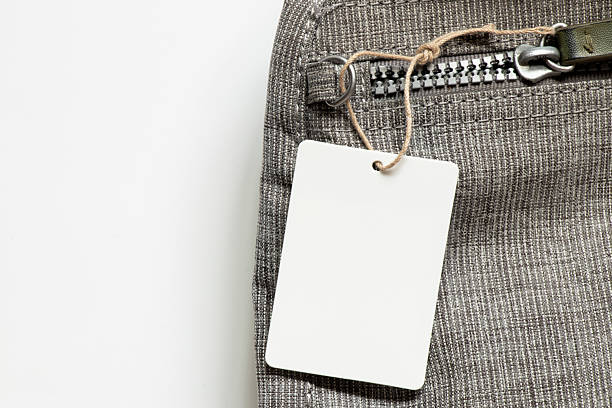 White blank tag on rope lies on gray backpack on white background as mockup for design close-up
