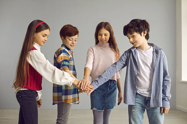 Group of preteen children standing together and pile up hands palm for integration and team spirit demonstration. Kids teambuilding, teamwork and cooperation concept. Studio shot on copy space