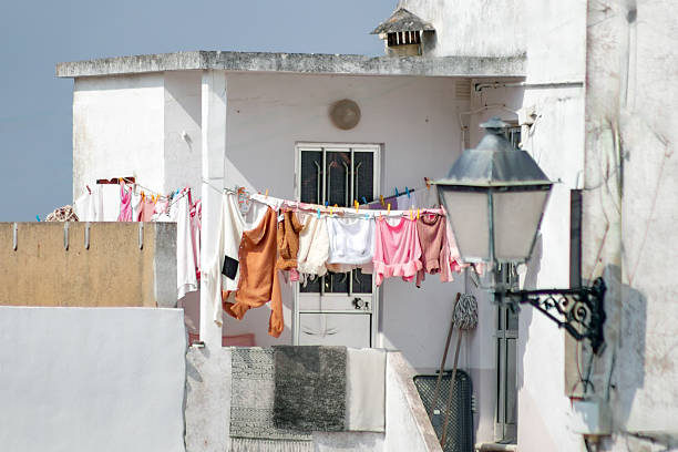 Colorful clothes hanging on a line to dry outside a balcony in Portugal. This everyday street scene with laundry, whitewashed walls, and a vintage lantern reflects Mediterranean lifestyle and local traditions.