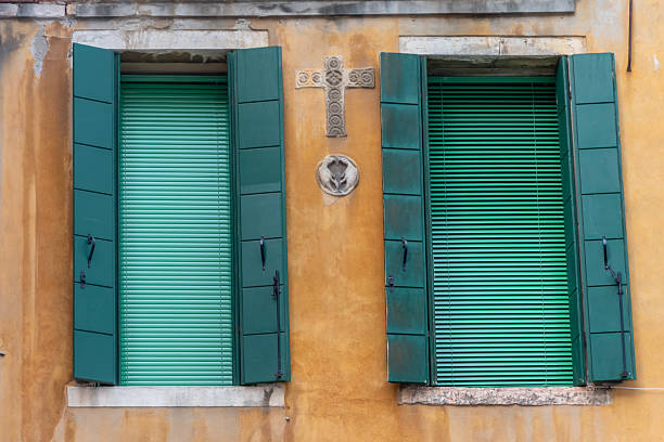 Green shutters on a yellow wall with a decorative cross