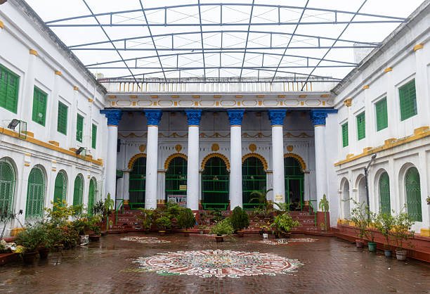 Courtyard view of the historic Srirampur Dey Raj Bari in West Bengal, featuring tall Corinthian-style columns, arched windows, and vibrant rangoli on the floor. The colorful blue, green, and yellow accents highlight Indo-European architectural fusion. A cultural landmark symbolizing tradition, artistry, and the grandeur of Bengal’s heritage mansions.