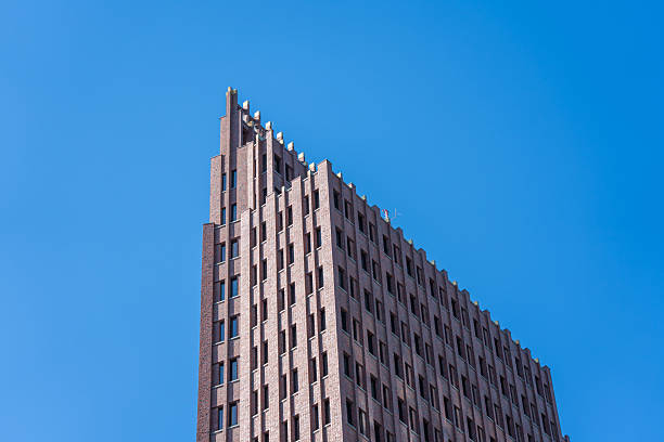 A red brick high-rise stands against a bright blue sky. Its architecture appears angular and massive.