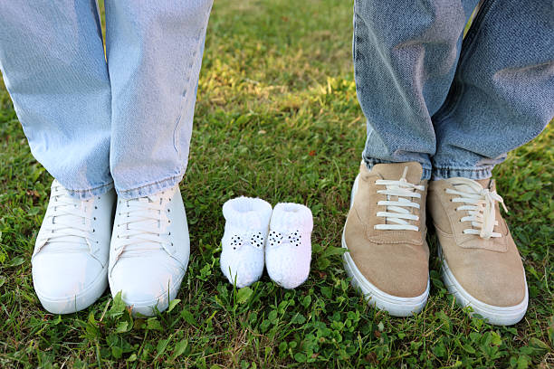 istock Couple's shoes on grass with tiny baby booties in middle, creative pregnancy announcement family photo. 2234542709