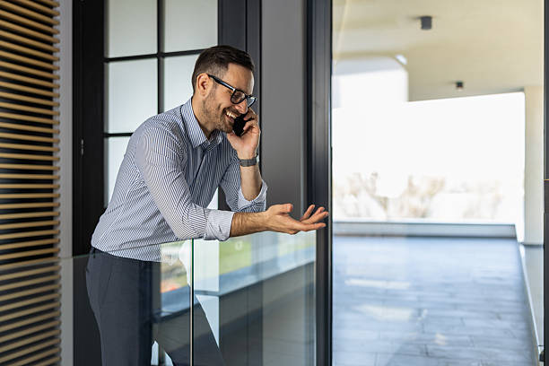 istock Business professional engaged in a phone conversation while standing in a modern office space with large windows 2234551328