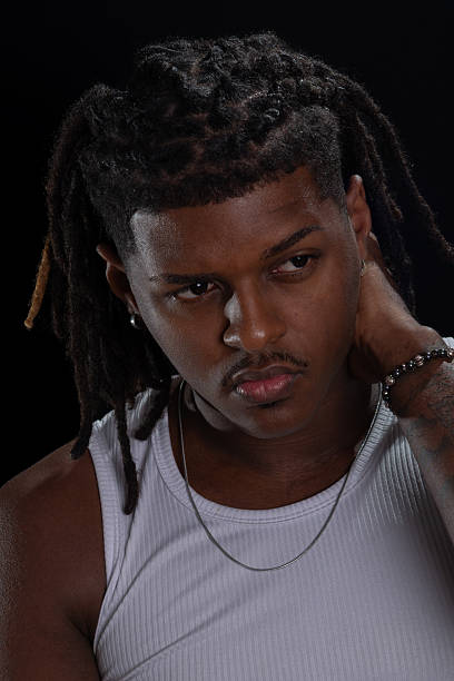 istock Handsome young man with dreadlocks and hands on his neck posing for a studio photo against a black background. Salvador, Brazil. 2234554180