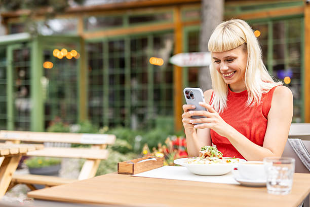 istock Smiling woman using smartphone while having lunch at outdoor cafe 2234558391