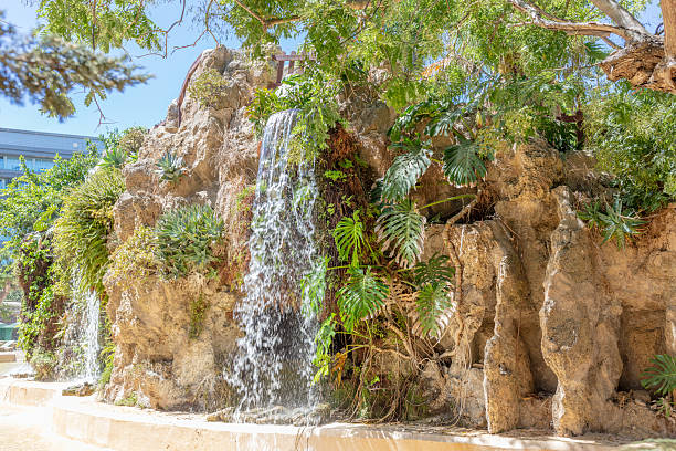 Artificial waterfall surrounded by lush greenery in a city park. Cadiz, Andalusia, Spain, September 2025. High quality photo