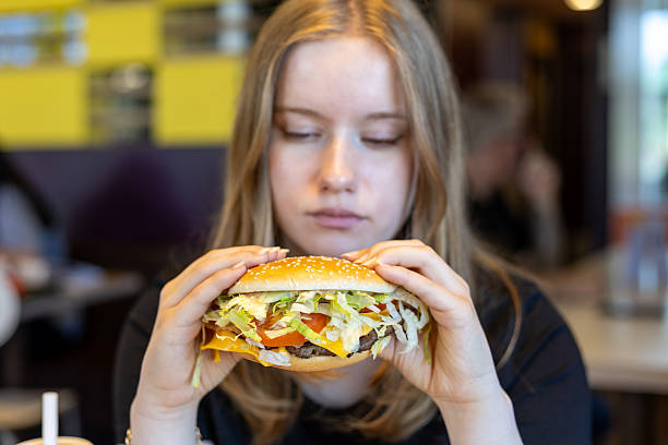 istock Young woman enjoys a large hamburger with fresh ingredients in a casual dining setting during lunchtime 2234561296
