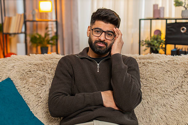 istock Indian young man looks into camera with serious empathetic face on sofa at home, expressing warmth 2234571157