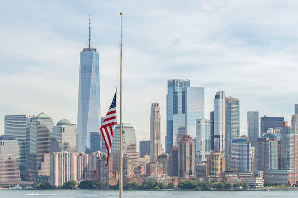 A view of the World Trade Center from Ellis Island with a US Flag visible next to it, signifying the past and present state of the WTC complex before and after the events of September 11th, 2001