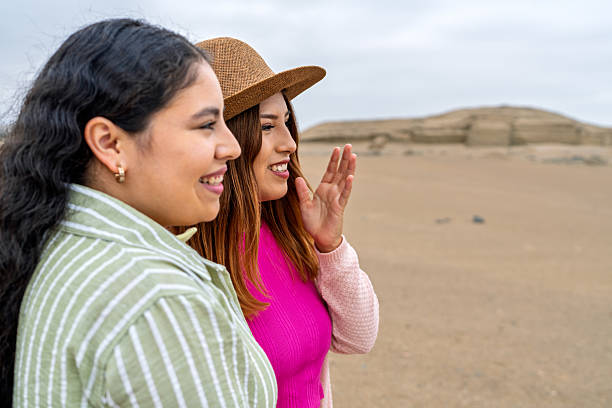 Two young women visiting pre-inca ruins in a sunny desert, admiring the ancient chimu culture and enjoying the breathtaking scenery