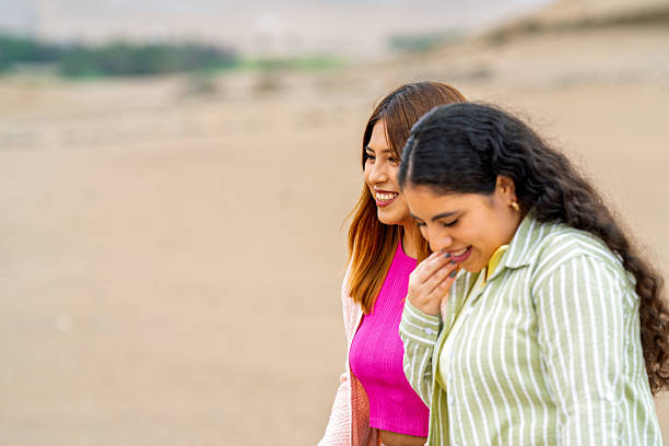 Two young women smiling and walking together near ancient pre-inca ruins in the stunning desert landscape of peru, enjoying their adventure