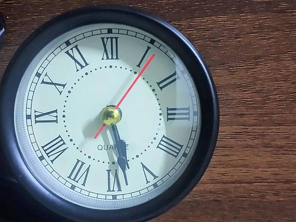 istock A vintage-style quartz clock with classic Roman numerals, telling time on a rustic wooden background. 2234594580