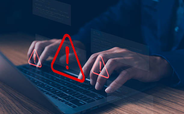 istock Person typing on laptop with red warning signs and holographic code, symbolizing critical programming errors, cybersecurity threats, or data breach risks in a digital work environment. 2234594905