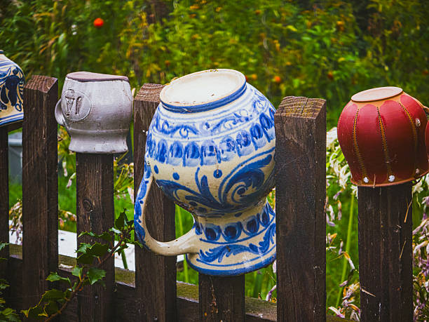 Close-up of colorful ceramic mugs and pots placed upside down on a rustic wooden fence in a countryside garden, representing folk culture, rural tradition and heritage, while creating a decorative rustic texture and pattern background,
