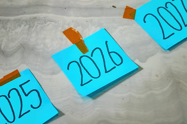 Three blue sticky notes labeled 2025, 2026, and 2027 taped to white marble surface with brown tape symbolizing timeline, planning, and new year goals in a creative layout.
