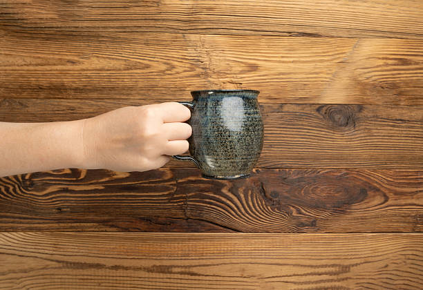 istock Hand Holds Cup, Empty Cup in Hands, Coffee Mug, Teacup Mockup, Cup in Arms on Wooden Table 2234603322