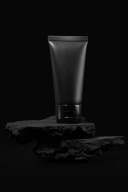 Black plastic cream tube with stone for mockup on black background. Selective Focus.