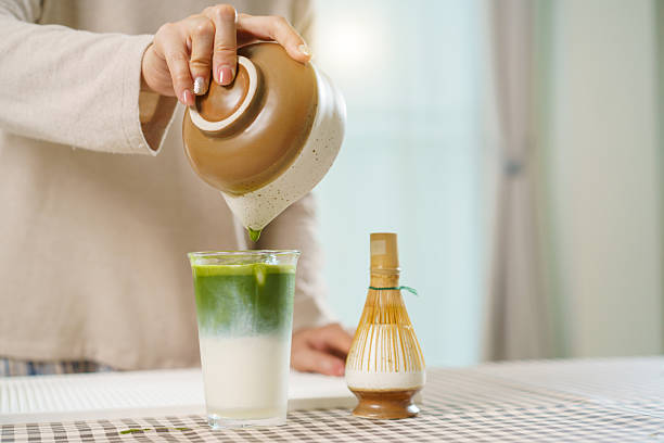 Asian woman preparing traditional Japanese matcha tea at home using bamboo tools, sifting matcha powder with care and precision.