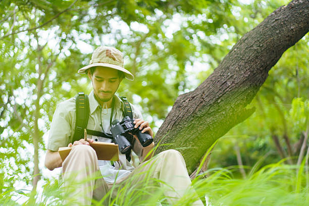 istock Asian man birdwatching with binoculars and notebook, studying wildlife in nature. 2234609665