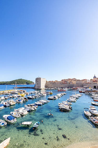 Small boats docked in a sunny harbor beside ancient stone city walls and historic buildings. Coastal town with vibrant waterfront, tourism, and maritime lifestyle. Scenic port with boats and architecture.