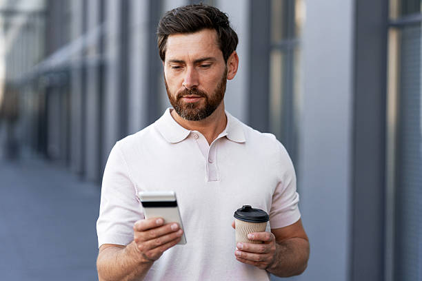 istock Businessman reading messages on smartphone while holding coffee outside office building 2234615914