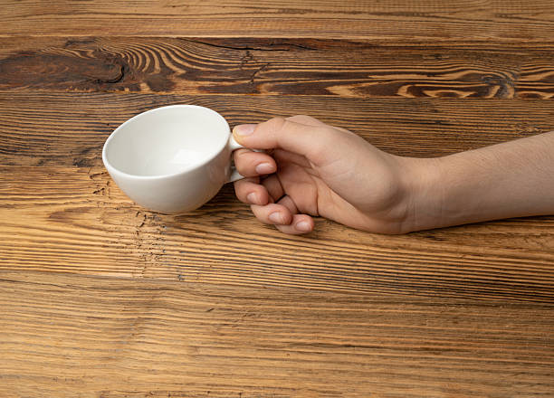 istock Hand Holds Cup, Empty White Cup in Hands, Coffee Mug, Teacup Mockup, Cup in Arms on Wooden Table 2234616354