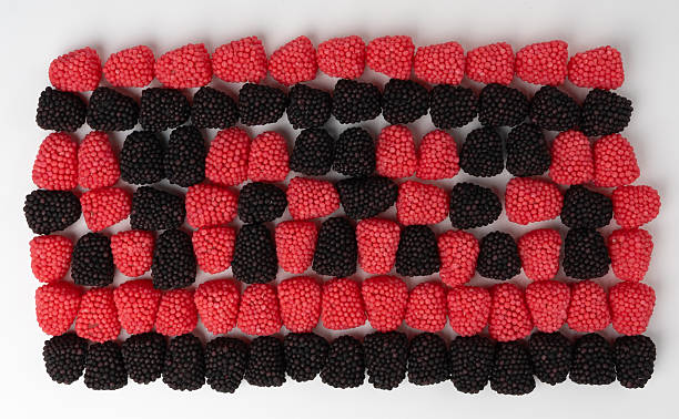 Gummy candies in red and black colors are artistically scattered on a soft pink surface, showcasing their textured surfaces in a fun and inviting way.