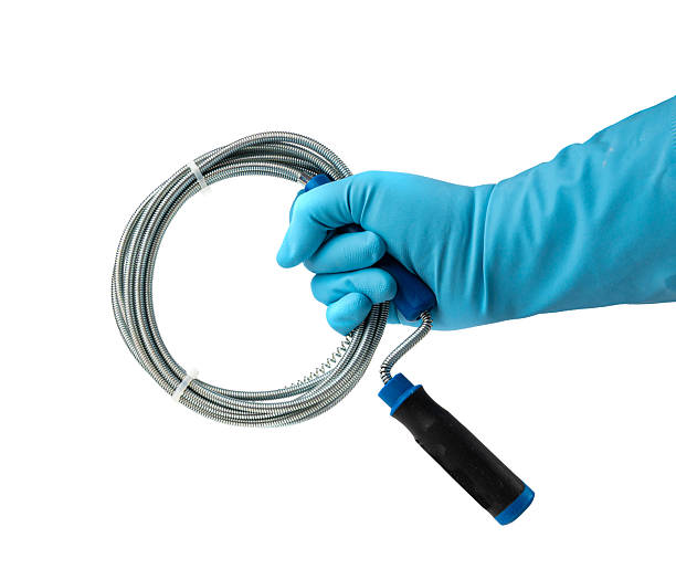 Metal drain auger tool isolated, plumbing snake or cable in hands in blue glove on white background, removing sink blockages