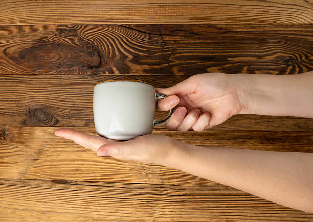 istock Hand Holds Cup, Empty Cup in Hands, Coffee Mug, Teacup Mockup, Cup in Arms on Wooden Table 2234618217