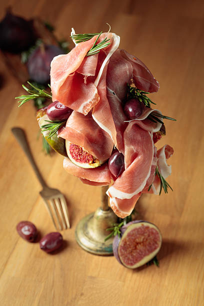 Prosciutto with figs, rosemary, and red olives on a old wooden table.