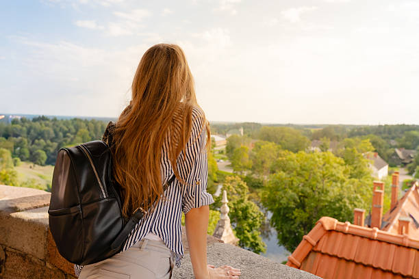 Young woman with backpack enjoys panoramic view over rooftops, forest and horizon, capturing the spirit of travel and exploration.
