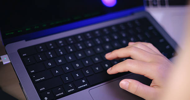 Close up shot, A woman's hands are typing on a laptop keyboard at a desk in a home office at night.
