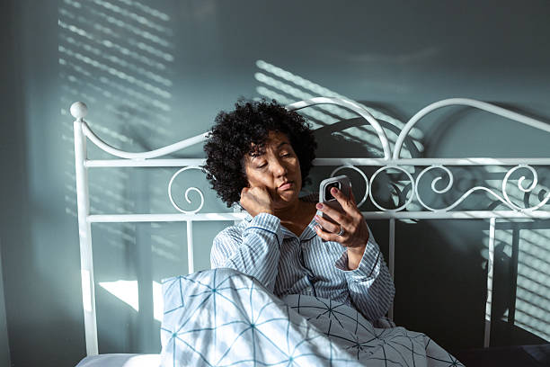 istock Woman sitting on a bed looking at smartphone in daylight 2234629494