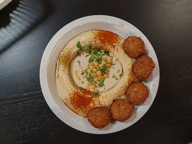 Personal perspective of a young multiracial woman eating vegan tempeh falafels in a wood bowl with cooked pumpkin, salad, tzatziki, and dressing.  Bali, Indonesia.