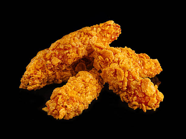 Crispy fried chicken tenders stacked on a dark surface