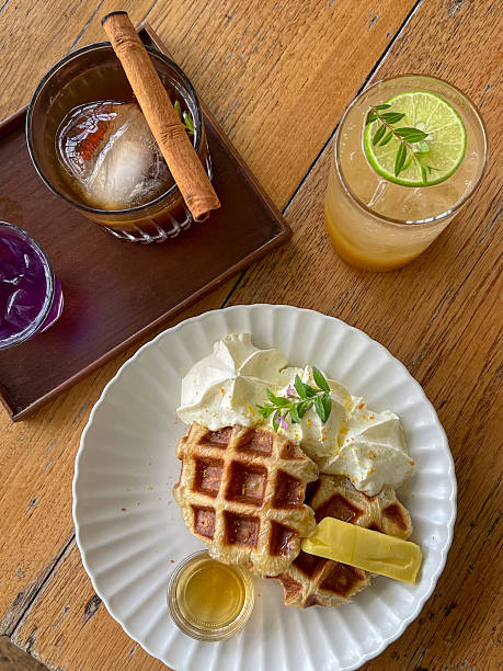 A caramel waffle whipped cream maple syrup butter cinnamon stick iced coffee citrus drink lime wooden table brunch delight. cozy cafe brunch with