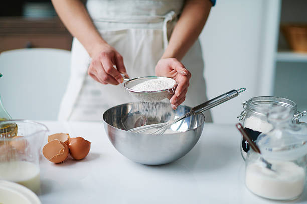 istock Anonymous Woman Sifting Flour into Mixing Bowl While Baking 2234641451