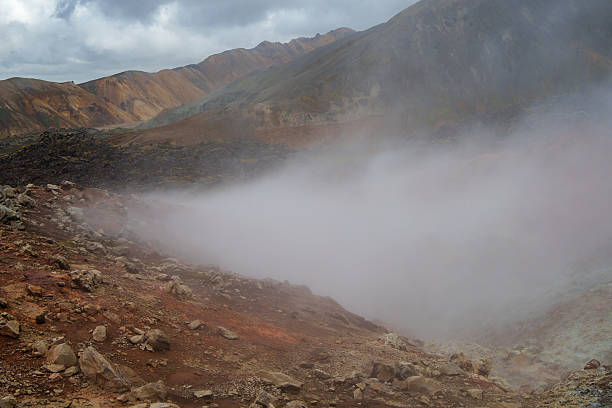Geothermal area emitting steam and smoke with colorful rhyolite mountains in the background, in iceland, creating a dramatic and otherworldly landscape