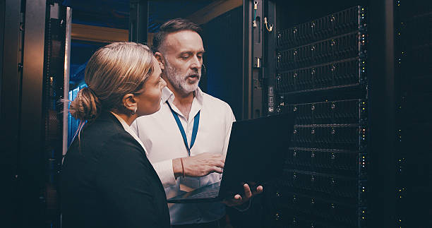 istock Server room, talking and people on laptop for technical support, network maintenance and database. IT technicians, team and man with woman on computer for diagnostics, system update and cybersecurity 2234648717