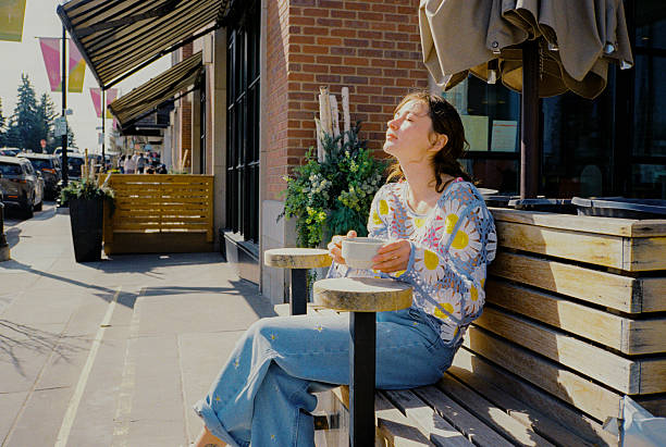 Woman drinking coffee sitting  in sidewalk cafe on sunshine  on first warm days. Shot on camera film