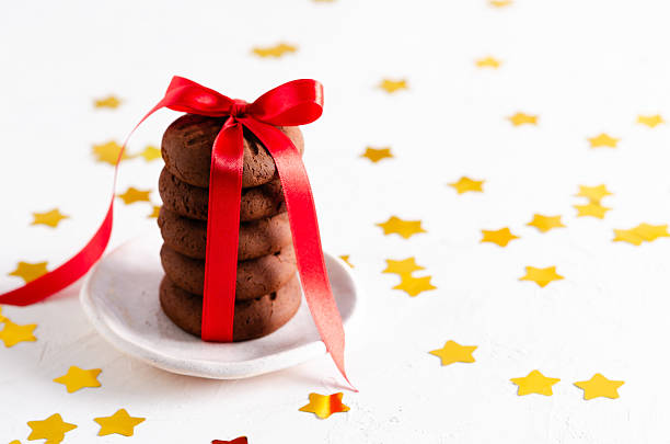 Stacked chocolate cookies tied with a red ribbon and golden stars on white background. Horizontal format and copy space.