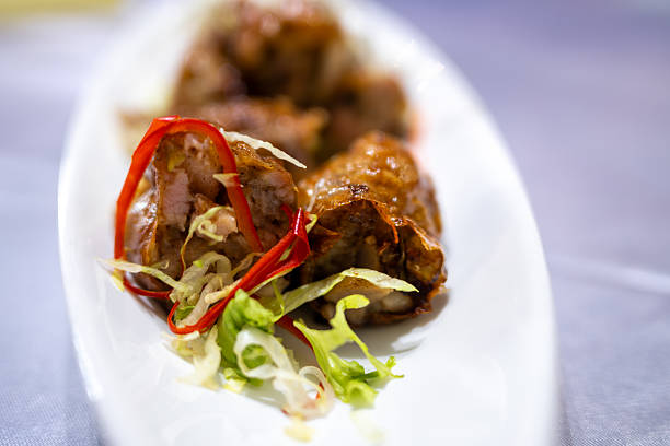 Grilled Meat Rolls with Red Pepper and Lettuce Garnish Served on a White Platter