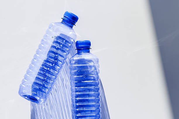 istock Transparent plastic bottles with blue caps and sun shadows on light background. Top view Water bottles at natural light. Themes of recycling, sustainability, water conservation, minimal style 2234661464