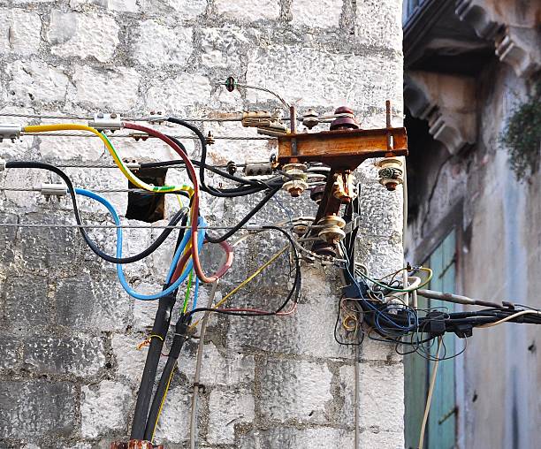 istock Tangled utility wires and rusty bracket on old stone wall 2234663974