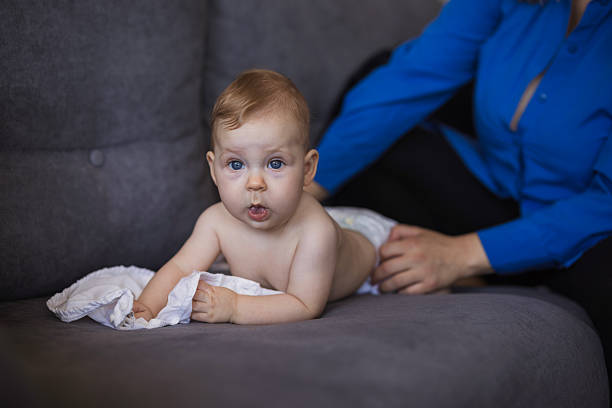 Baby lying on its stomach on a sofa while its mother changes its diaper