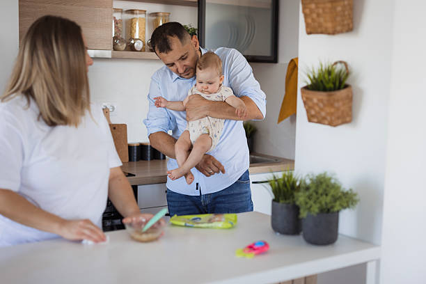 istock Father holding baby while mother is preparing food in kitchen 2234668376