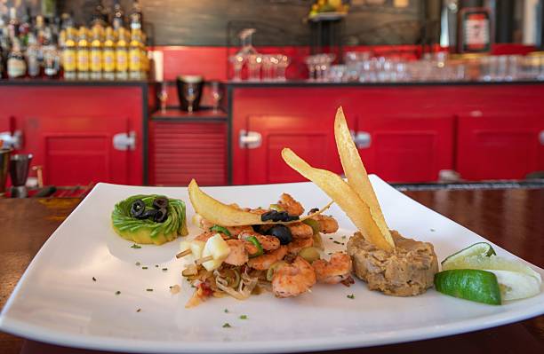 Gourmet shrimp dish with avocado and lime on a white plate in a vibrant red restaurant setting.